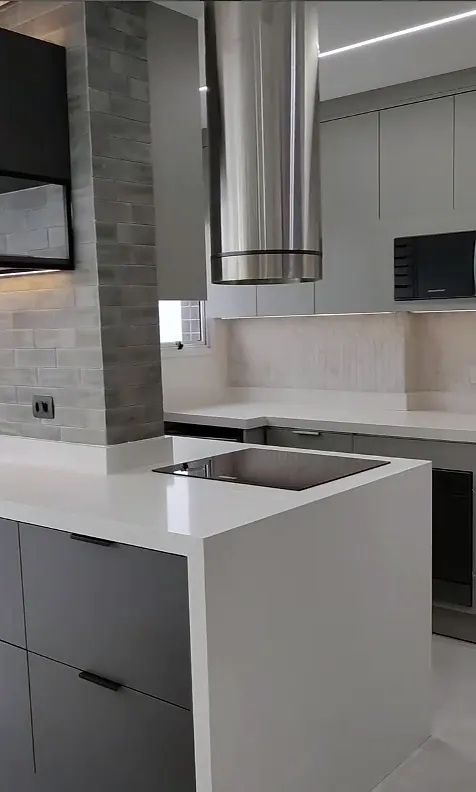 Ilha de bancada branca com cooktop, coifa de inox e pilar revestido em pedra cinza