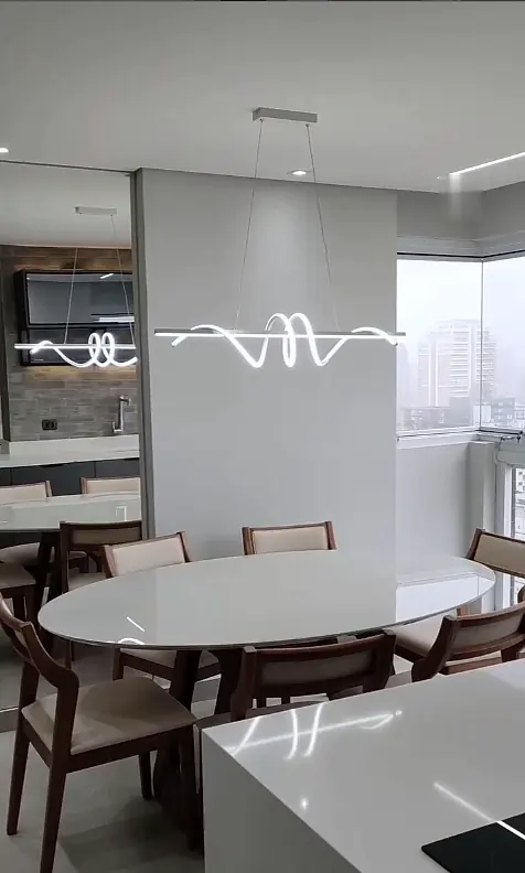 Sala de jantar com mesa oval branca, cadeiras de madeira e pendente de LED ondulado
