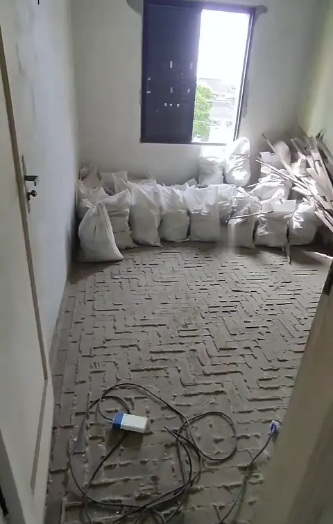 Quarto em obra com sacos de entulho e piso descascado