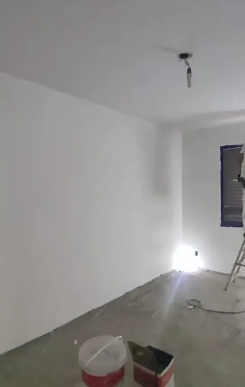 Cômodo com paredes brancas lisas, contrapiso aparente e baldes de material