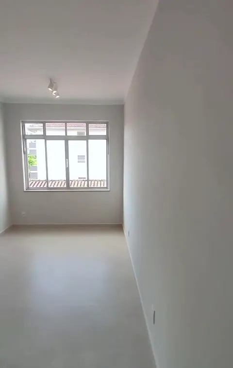 Sala vazia reformada, com piso claro, paredes brancas e janela ao fundo