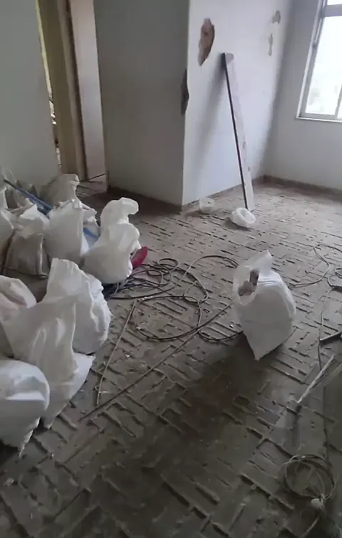 Cômodo em demolição com sacos de entulho, fios soltos e contrapiso exposto
